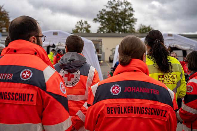 Das Bild zeigt Helfende von DRK, Johanniter und ASB von hinten in Einsatzkleidung.