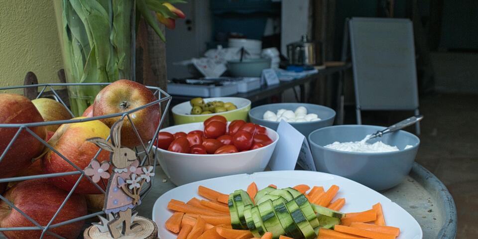 Tisch mit Fingerfood für Teilnehmende des Ferienprogramms. Möhren, Gurken, Mozzarella, Oliven verschiedene Dipps, Cocktailtomaten, Äpfel