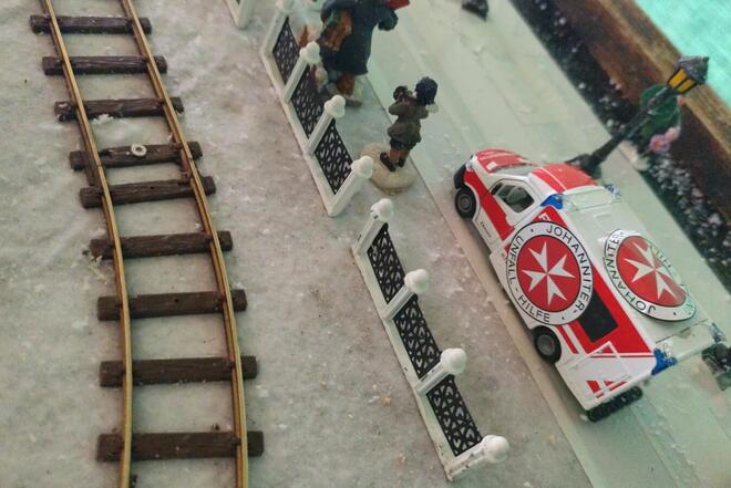 Ein kleines Spielzeug Johanniter Einsatzfahrzeug steht in einer Winter-Miniaturlandschaft.