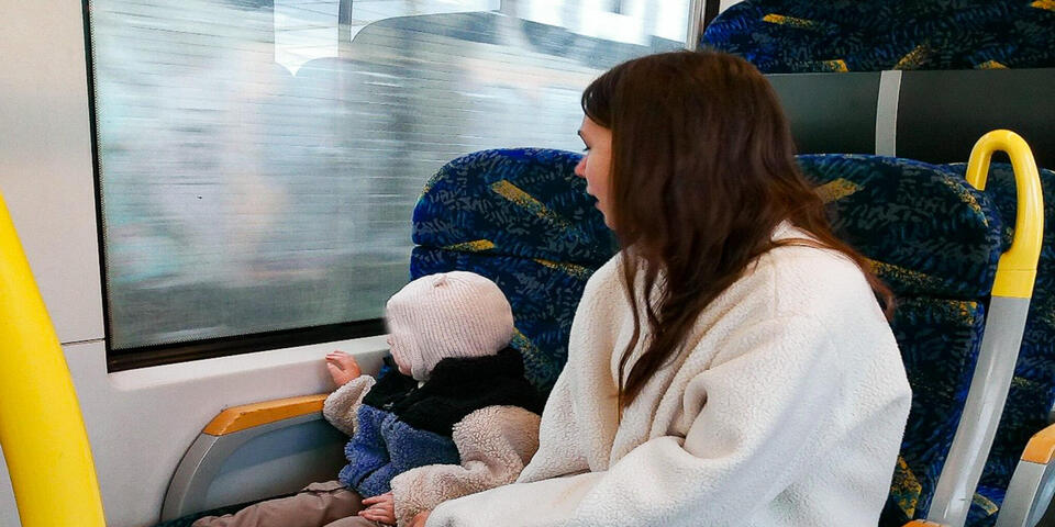 Eine Frau mit einem Kleinkind in einem Linienbus. Das Kind schaut aus dem Fenster.