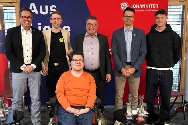 Jahnler und Mitarbeitende der Johanniter vor einer Pressewand.