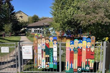 Bein Sonnenschein erstrahlt die Kita Hoppetosse mit buntem Zaun davor, den die Kinder selbst gestaltet haben.