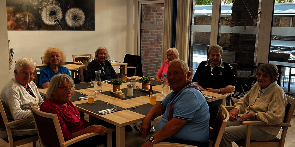 eine Gruppe Senioren sitzt um einen Tisch und blickt lächelnd zur Kamera