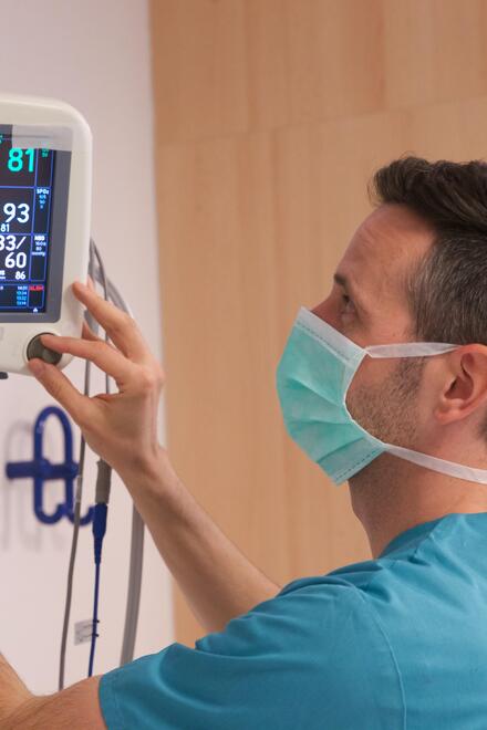 Pflegekraft mit Mundschutz stellt Patientenmonitor ein.