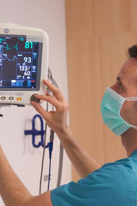 Pflegekraft mit Mundschutz stellt Patientenmonitor ein.