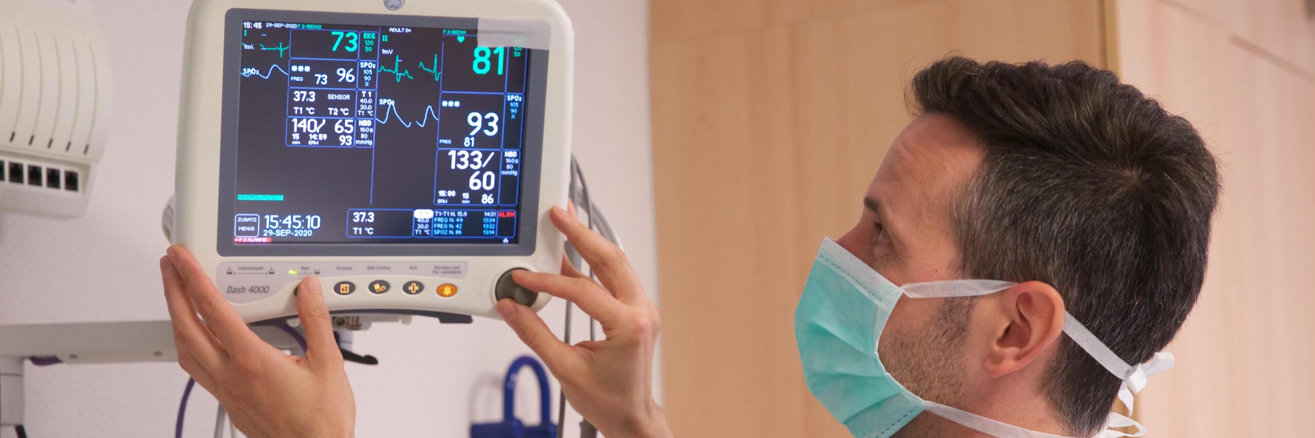 Pflegekraft mit Mundschutz stellt Patientenmonitor ein.