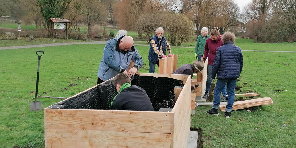 Menschen bauen Hochbeete in einem Park zusammen