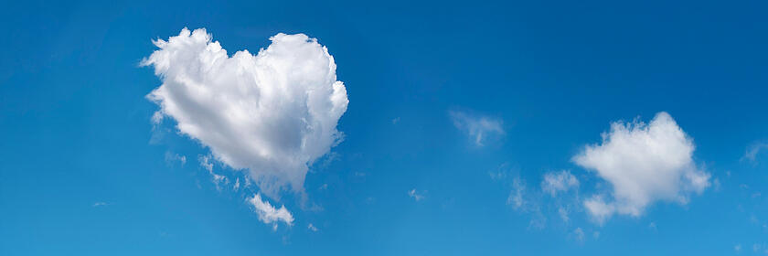 Eine weiße Wolke in Herzform schwebt am klaren blauen Himmel.