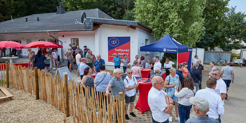 Menschen feiern unter roten Sonnenschirmen die Eröffnung vom Treffpunkt "vor Müllert"