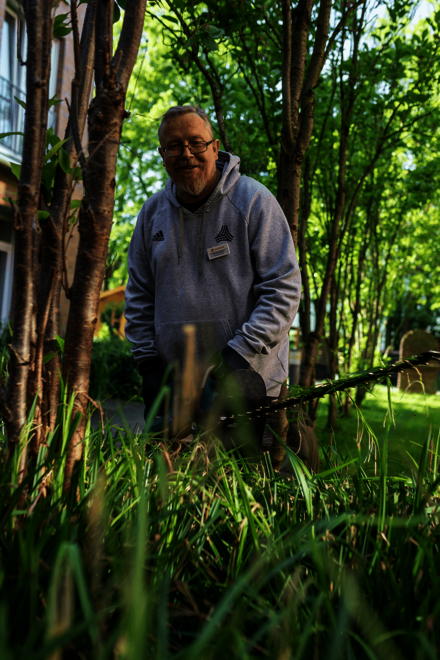 Ein Mann in grauer Arbeitskleidung schneidet im Garten mit einer Heckenschere Pflanzen