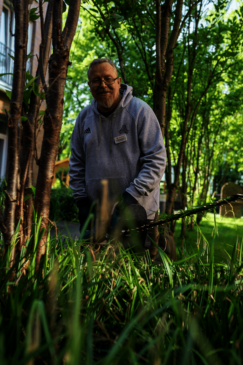 Ein Mann in grauer Arbeitskleidung schneidet im Garten mit einer Heckenschere Pflanzen