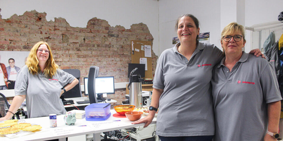 Eine Frau hinter einem Tisch mit Essen. Zwie Frauen davor.