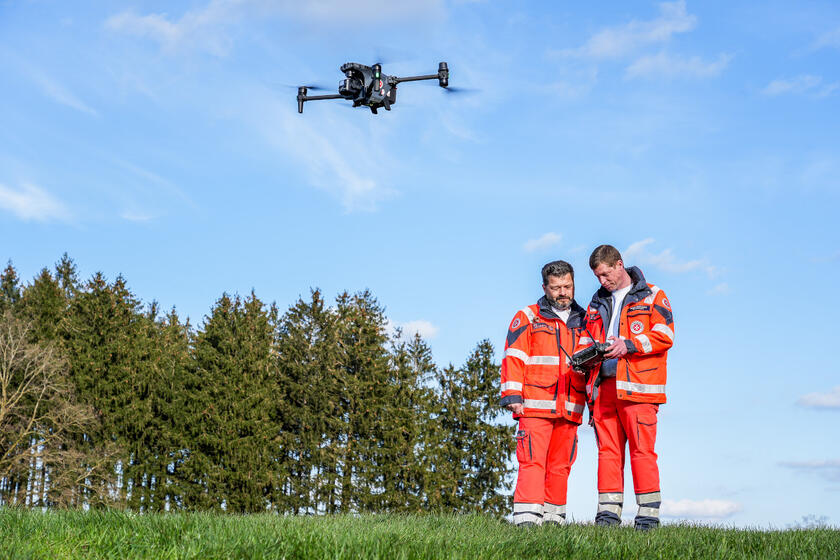 Zwei Johanniter Rettungskräfte steuern eine Drohne über einem Feld.