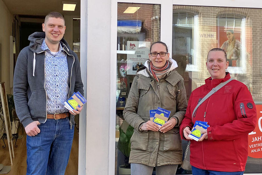 Ein mann und zwei Frauen halten auffällige Aufkleber in den Händen