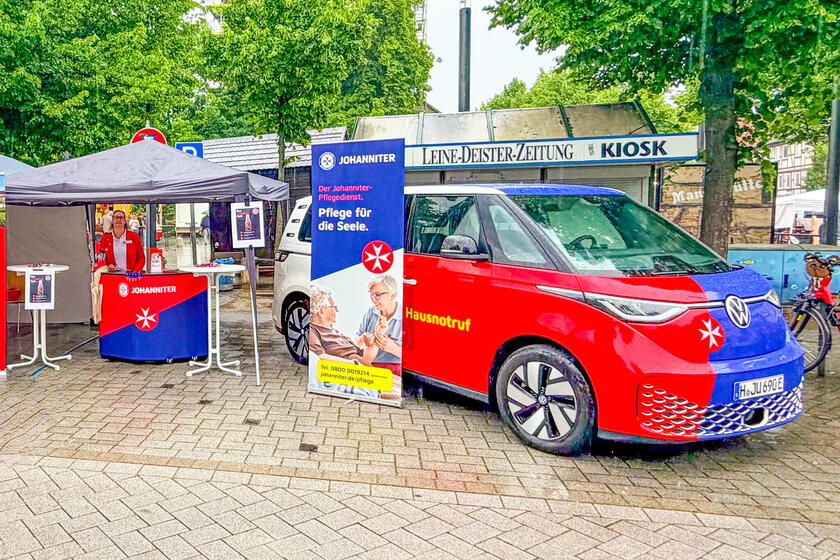 Eine Frau steht an einem Messestand unter einem Pavillon. Daneben ein Roll-Up und ein Bulli. Alle mit Johanniter-Logo.