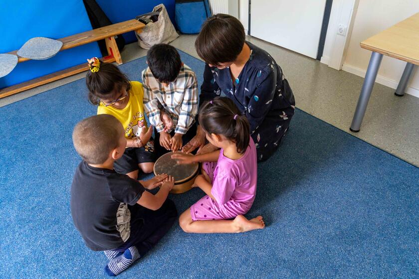Eine Frau und vier Kinder sitzen um eine kleine Handtrommel herum und schlagen mit den Fingern darauf.