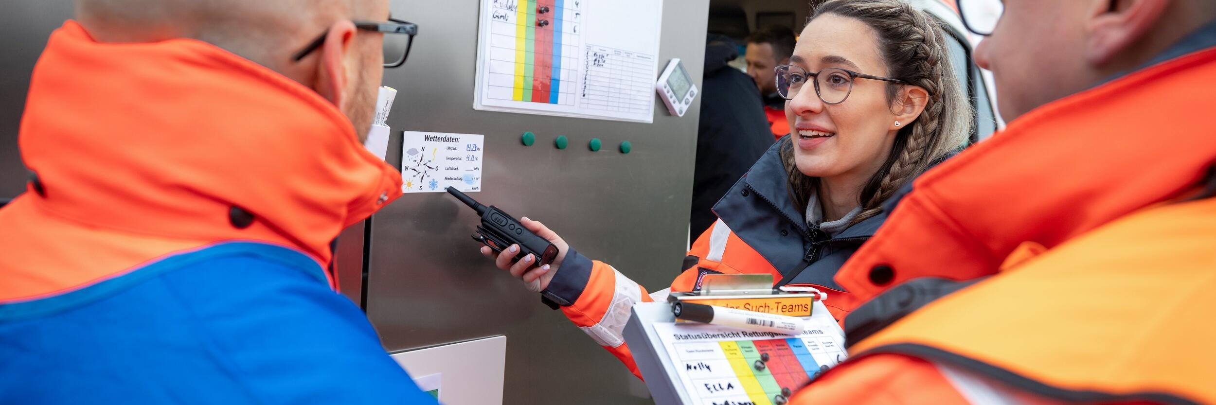 Bevölkerungsschutz: Ehrenamtliche stehen vor einem Rettungsfahrzeug und schauen auf einen Plan.