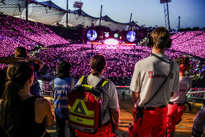 Sanitätskräfte blicken auf leuchtende Menschenmenge bei Konzert im Olympiastadion