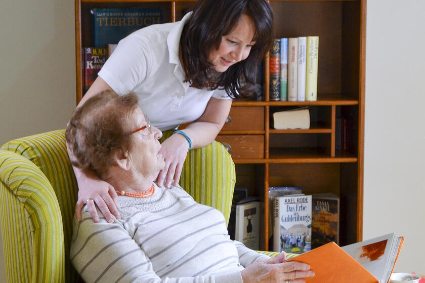 Eine Mitarbeiterin der Johanniter-Tagespflege in Ahrensburg spricht mit einem Gast über ein Buch.
