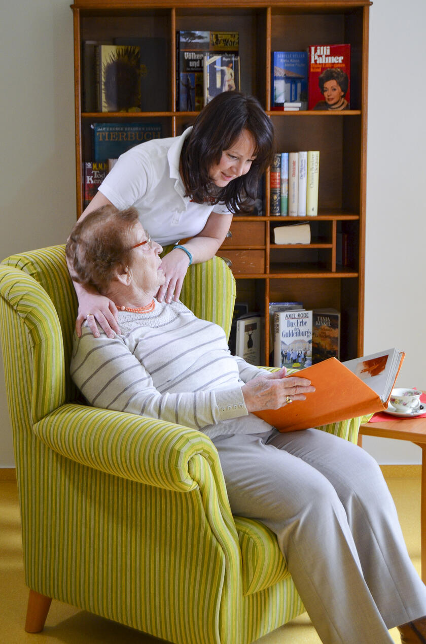 Eine Mitarbeiterin der Johanniter-Tagespflege in Ahrensburg spricht mit einem Gast über ein Buch.