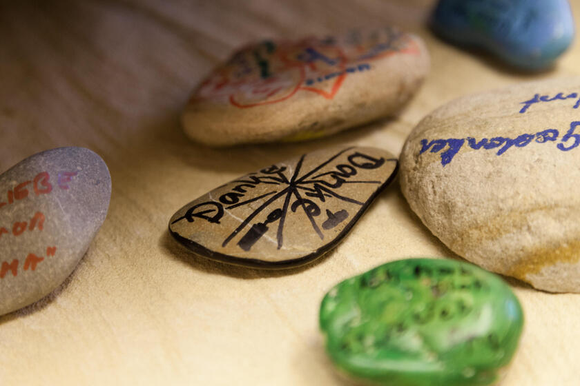 mehrere Kieselsteine liegen auf einem Tisch, die als Erinnerungssteine beschrieben oder bemalt sind