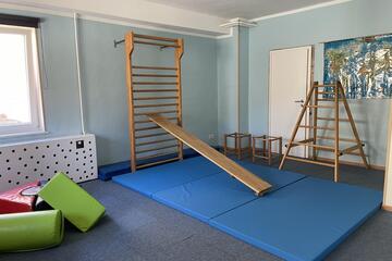 Ein Raum mit Turnmatten, einer Kletterwand sowie einer Bankrutsche und Sitzpolster.