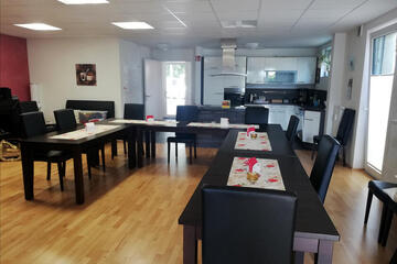 Zahlreiche Tische und Stühle und im Hintergrund ist die offen gestaltete Küche zu sehen.