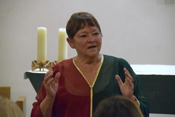 Magdalena Janotte steht im roten Kleid vor dem Altar und gestikuliert.