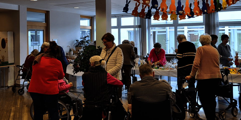 Menschen mit und ohne Rollstuhl unterhalten sich oder betrachten das Angebot auf den Basartischen.