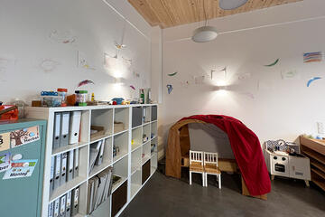Heller Gruppenraum mit Bücherregal links an der Wand. Eine Lese-Kuschelecke mit Sitzmöglichkeit unter einem Stoffhimmel.