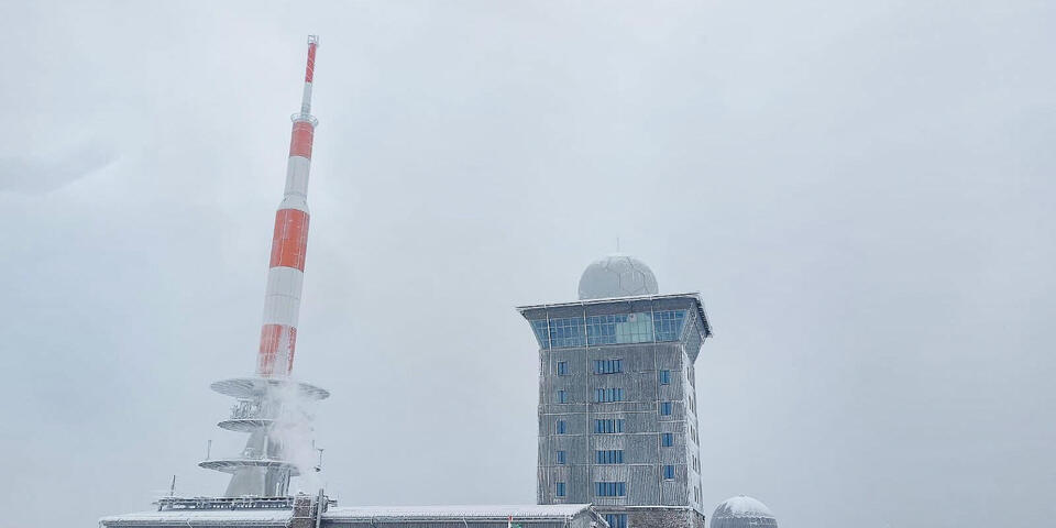 Die große Kuppel und ein hoher Funkturm auf einem verschneiten Berggipfel.