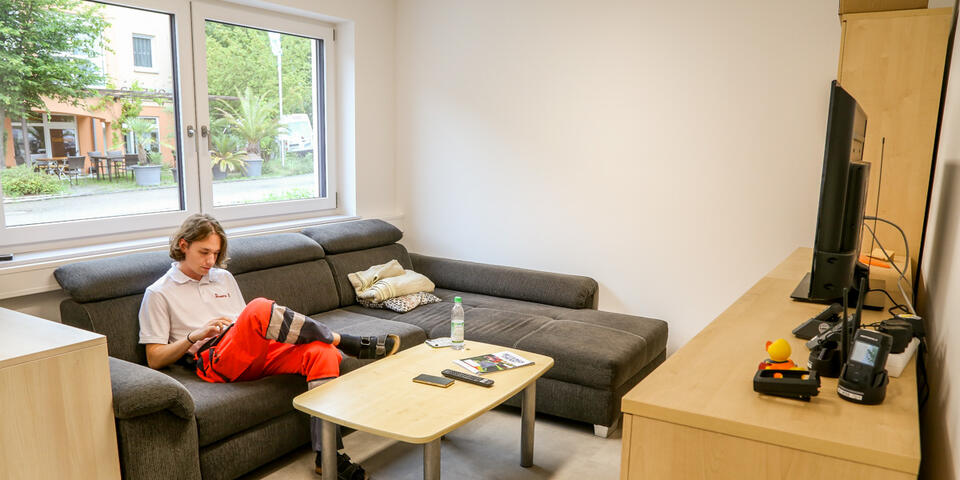 Einsatzkraft im Aufenthaltsraum auf dem Sofa sitzend an einem Tablet.