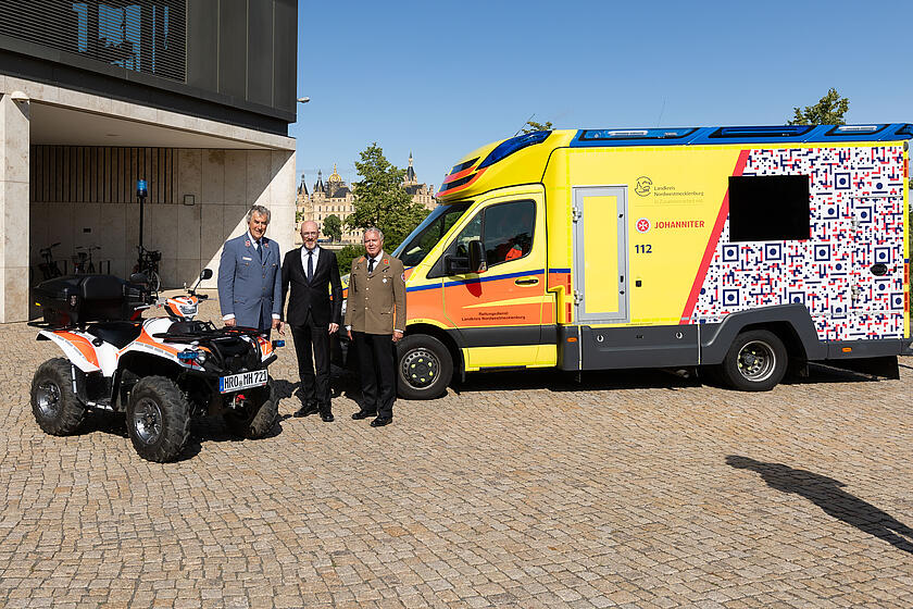 Auf dem Bild sind drei Personen zu sehen (Georg Khevenhüller, Christian Pegel, Volker Bescht) stehend neben zwei Einsatzfahrzeugen