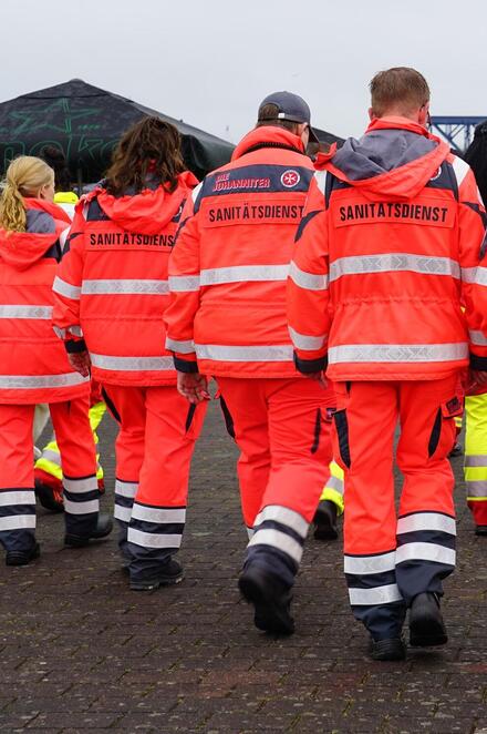 Zu sehen sind sieben ehrenamtliche Helferinnen und Helfer in Dienstkleidung von hinten