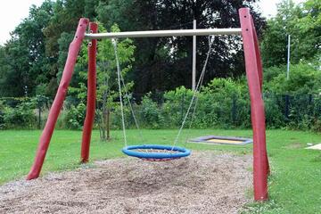 Vogelnestschaukel im Vordergrund, dahinter sieht man das Trampolin der Kita. 