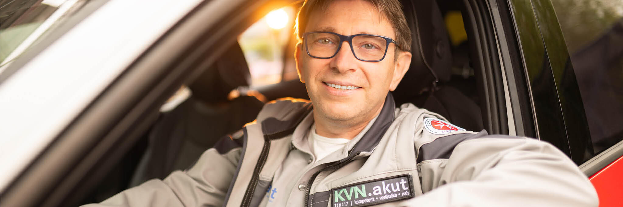 Ein Fahrer im ärztlichen Bereitschaftsdienst sitzt in einem Fahrzeug und schaut in die Kamera.