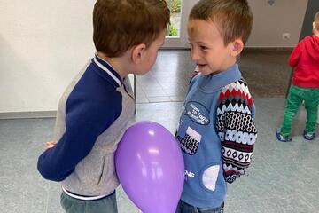 Zwei kleine Jungen halten einen Luftballon zwischen sich ohne die Hände zu benutzen.