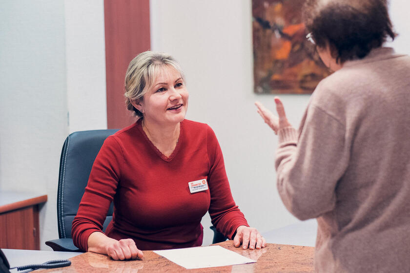 Frau im roten Pullover am Schreibtisch berät eine Bewohnerin