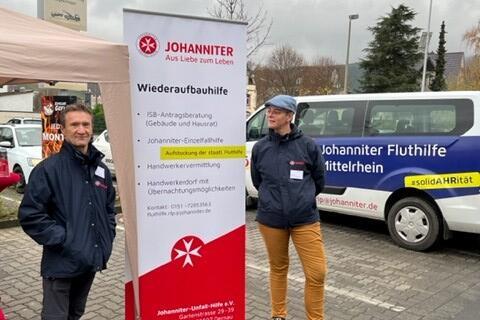 Zwei Mitarbeitende vor einem Roll-up der Johanniter-Fluthilfe