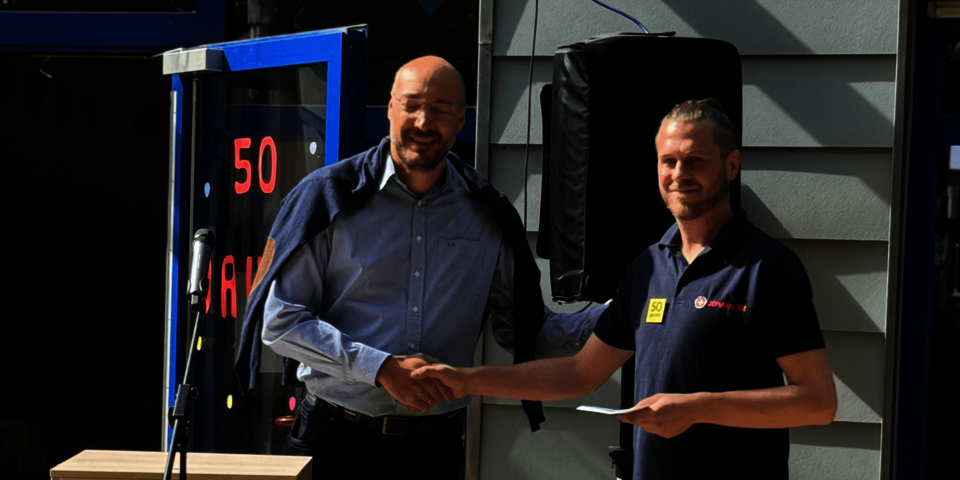   Zwei Männer schütteln sich bei einer Jubiläumsfeier die Hand und lächeln.