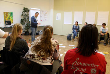 Ein Dozent steht in der Mitte, Jugendliche sitzen im Stuhlkreis und hören zu