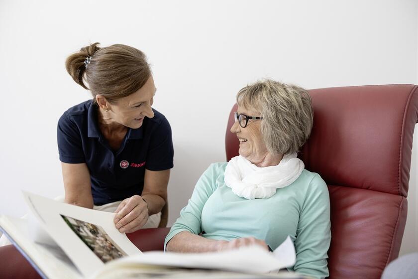 Eine Mitarbeiterin in der Tagespflege der Johanniter schaut gemeinsam mit einer Seniorin in ein Fotoalbum.