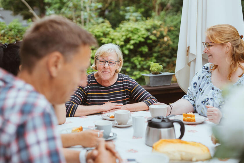 Eine ältere Dame sitzt mit ihrer Familie am Frühstückstisch.