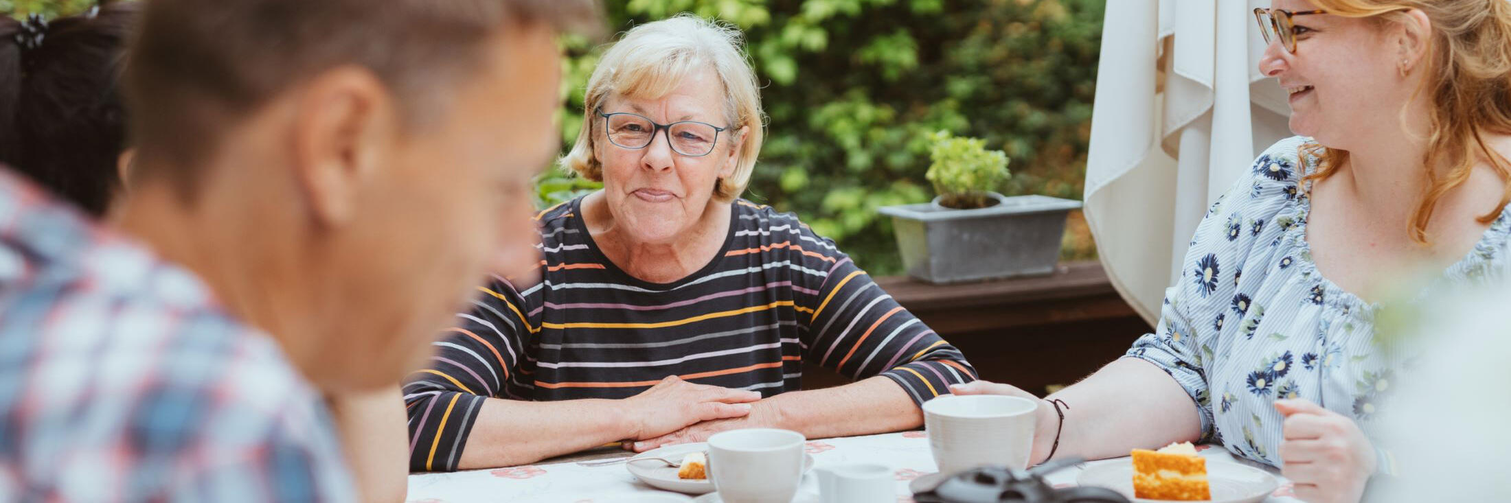 Eine ältere Dame sitzt mit ihrer Familie am Frühstückstisch.