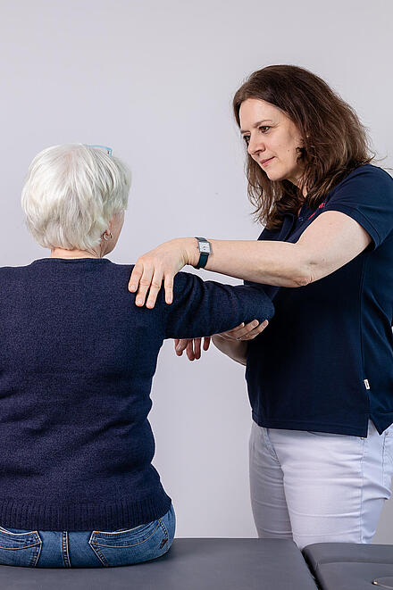 Eine Johanniterin führt eine Behandlung an der Schulter einer Patientin durch.