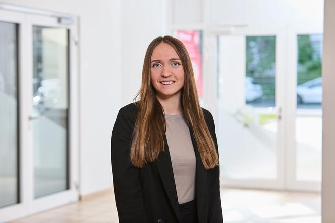 Eine Frau mit langen braunen Haaren einem hellbraunen Shirt und einem schwarzen Sakko