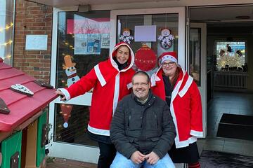 Der Leiter der Lokal zwei Mitarbeitende in Weihnachtsmann Verkleidung