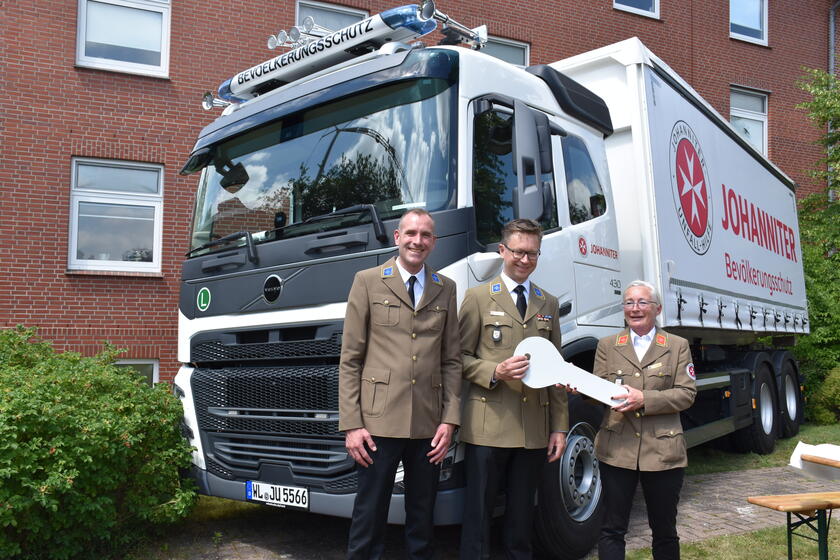Drei Personen stehen vor einem großen LKW aus dem Bevölkerungsschutz und halten einen symbolischen Schlüssel.