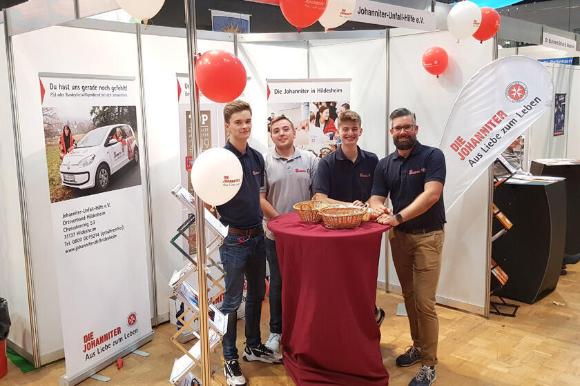 Johanniter stehen an ihrem Messestand und lächeln in die Kamera. 