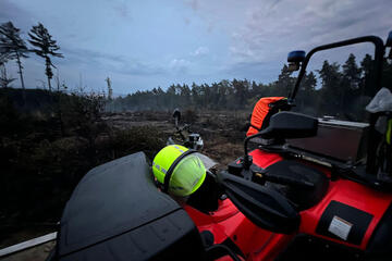Ein signalgelber Helm liegt auf einem Quad der Johanniter. Im Hintergrund sieht man verbrannte Erde.